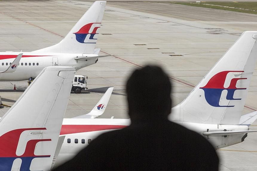 A silhouetted man looks out at aircraft operated by Malaysian Airline standing on the tarmac at Kuala Lumpur International Airport (KLIA) in Sepang, Malaysia, on Aug 26, 2014. -- PHOTO: BLOOMBERG