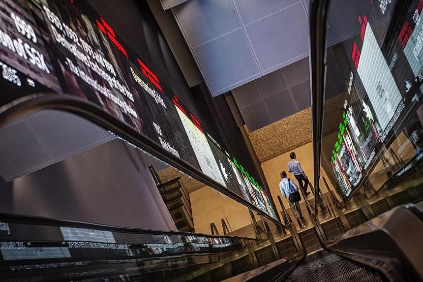 Pedestrians exiting an escalator that runs past an electronic screen and ticker board indicating stock figures at the Singapore Exchange Ltd. (SGX) headquarters in Singapore on Jan 21, 2015. -- PHOTO: BLOOMBERG