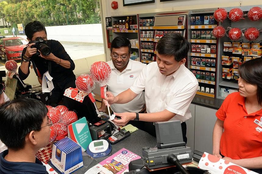 Minister Chan Chun Sing showing the SG50 little red dot to a customer at a petrol station. Motorists can celebrate the nation's 50th birthday and do their part for charity by buying "red dots" and decorating their cars with them. -- ST PHOTO: AZIZ HU