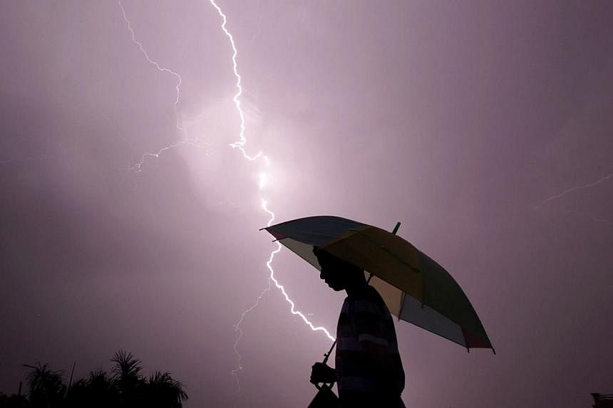 A pedestrian walking with an umbrella as lightning strikes during an evening thunderstorm in Jammu on May 14, 2015. -- PHOTO: AFP