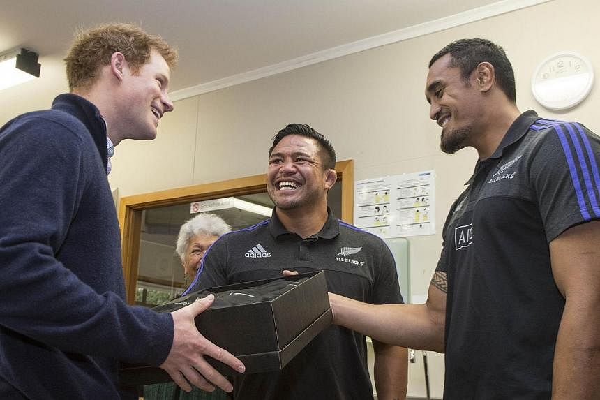 Britain's Prince Harry (left) is presented with an New Zealand All Black rugby jersey by All Blacks Jerome Kaino (right) and Keven Mealamu (centre) on a visit to the Auckland Spinal Rehabilitation Unit in Auckland on May 15, 2015. -- PHOTO: AFP&nbsp;
