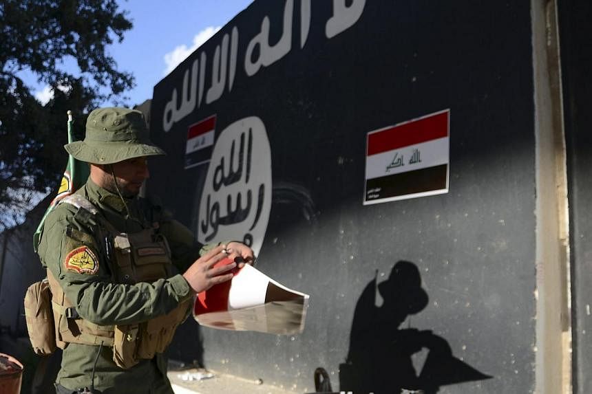 A Shi'ite paramilitary fighter puts Iraqi flags on a wall painted with the black flag commonly used by Islamic State militants in Tikrit March 31, 2015, after Iraqi troops aided by Shi'ite paramilitaries drove Islamic State out of central Tikrit. -- 