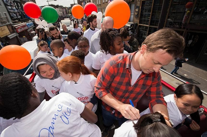 British chef and television presenter Jamie Oliver signs a child's shirt during an open-top bus tour of central London to promote Food Revolution Day on May 15, 2015. Jamie Oliver is calling for a global campaign to put compulsory practical food educ