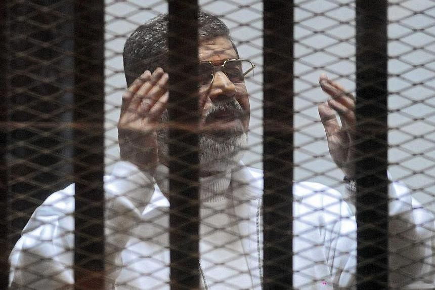 Ousted Egyptian President Mohamed Mursi gesturing from inside a cage in the courtroom where he stood trial in Cairo, Egypt on Feb 15, 2015. -- PHOTO: EPA&nbsp;