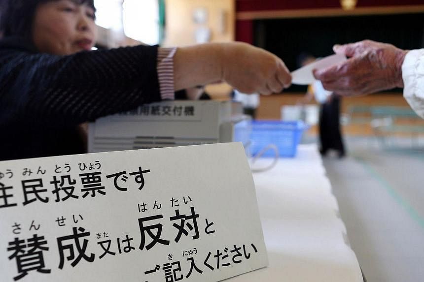 A resident (right) receives a ballot at a polling station in Osaka on May 17, 2015 to vote on a referendum to reform the city administration into a metropolitan government.&nbsp;The people of Japan's second city Osaka narrowly voted down Sunday a pla