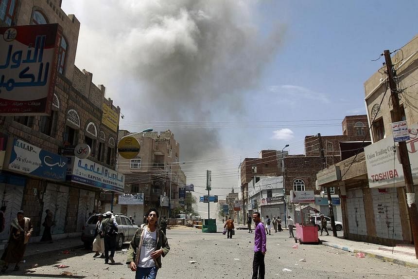 Yemeni men stand on a street as smoke billows following reported air strikes on the residence of Yemen's former president Ali Abdullah Saleh on May 10, 2015, in the capital Sana'a.&nbsp;Saudi-led coalition warplanes resumed strikes on the preisdienti