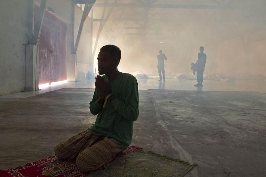 A rescued Bangladeshi migrant praying while Indonesian personnel fumigate a warehouse converted into sleeping quarters for migrants at a fishing port in Langsa, Aceh province, on May 19, 2015. The Philippines has said it is ready to accept migrants f