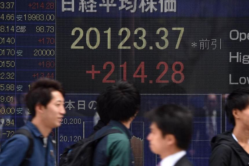 People walking past an electric quotation board flashing the numbers of the Nikkei key index at the Tokyo Stock Exchange (TSE) in front of a securities company in Tokyo. -- PHOTO: AFP
