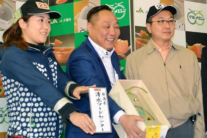 The successful bidder (centre) showing the pair of Yubari melons after this year's first auction at the Sapporo Central Wholesale Market in Sapporo on May 22, 2015. -- PHOTO: AFP&nbsp;