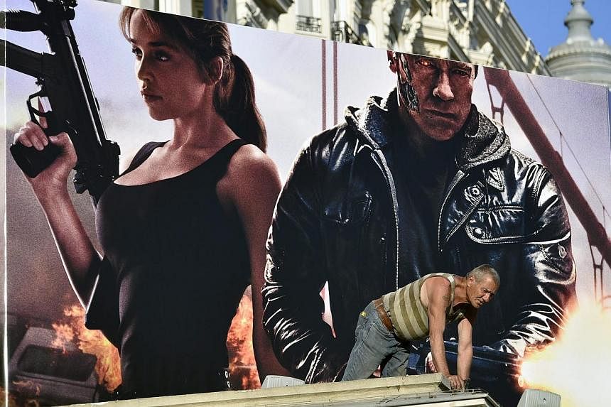 A worker is seen in front of a poster of Terminator Genisys showing cast members Arnold Schwarzenegger (right) and Emilia Clarke (left) at the Carlton Hotel, ahead of the 68th Cannes Film Festival, in Cannes, France, 12 May 2015. -- PHOTO: EPA