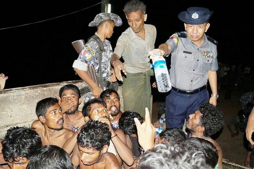A Myanmar police officer giving a water bottle to would-be migrants on a fishing boat off the western coast of Rakhine on May 22, 2015. -- PHOTO: AFP/MYANMAR INFORMATION MINISTRY