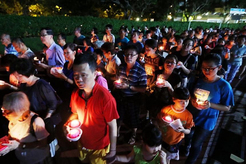 Buddhist devotees holding candles shaped like lotus flowers and praying for peace, at Hougang Stadium on May 24, 2015. -- PHOTO: LIANHE ZAOBAO