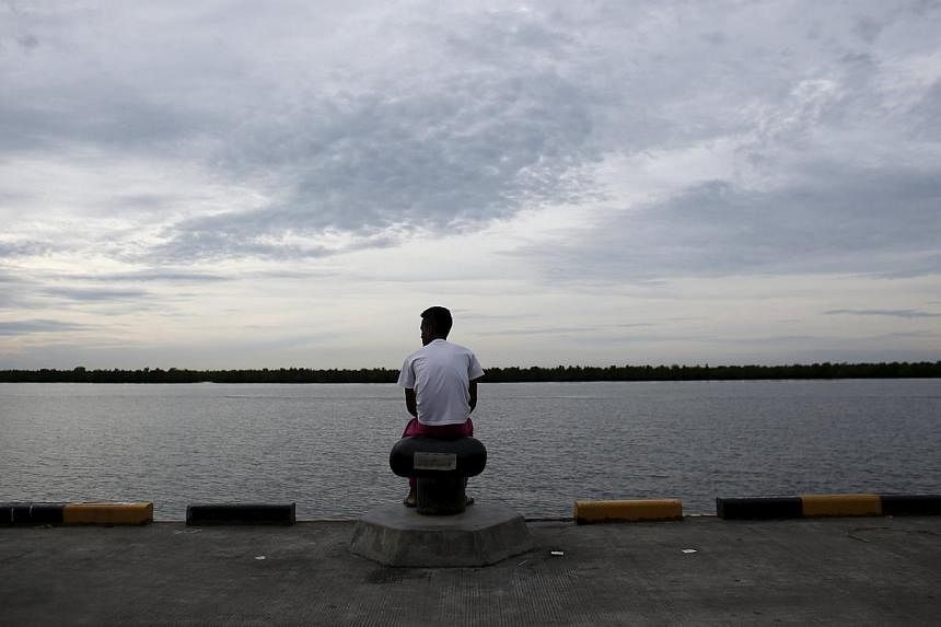 A Bangladeshi migrant who arrived recently by boat sits on a dock near a temporary shelter in Kuala Langsa, in Indonesia's Aceh Province May 25, 2015. Thailand has deployed a helicopter carrier in its waters to serve as a temporary medical and proces