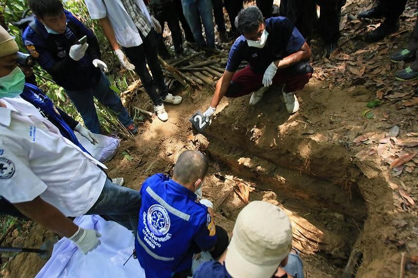 Rescue workers retrieve human remains from graves near the hillside site where shallow graves containing 26 bodies were found on May 1, close to the town of Padang Besar in the southern Thai province of Songkhla on May 13, 2015. -- PHOTO: AFP