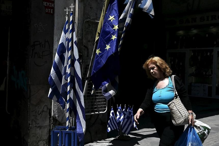 A woman carrying bags of goods makes her way past Greek national flags and European Union flags on display in Athens on May 25, 2015.&nbsp;Struggling Greece will keep on repaying its European Union-International Monetary Fund (IMF) creditors for as l