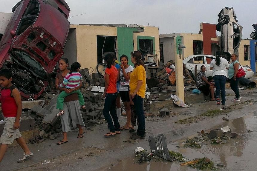 Residents stand outside their homes as damaged cars are seen after a tornado hit the town of Ciudad Acuna, state of Coahuila, May 25, 2015. At least 10 people died on Monday morning after a tornado hit Ciudad Acuna, a Mexican city on the border with 