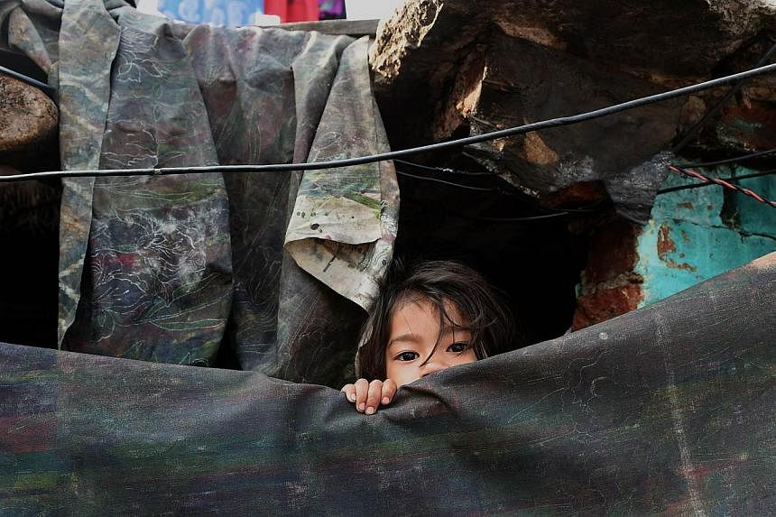 A young girl peeping out from her shanty in a slum in New Delhi on March 18, 2015. -- PHOTO: AFP