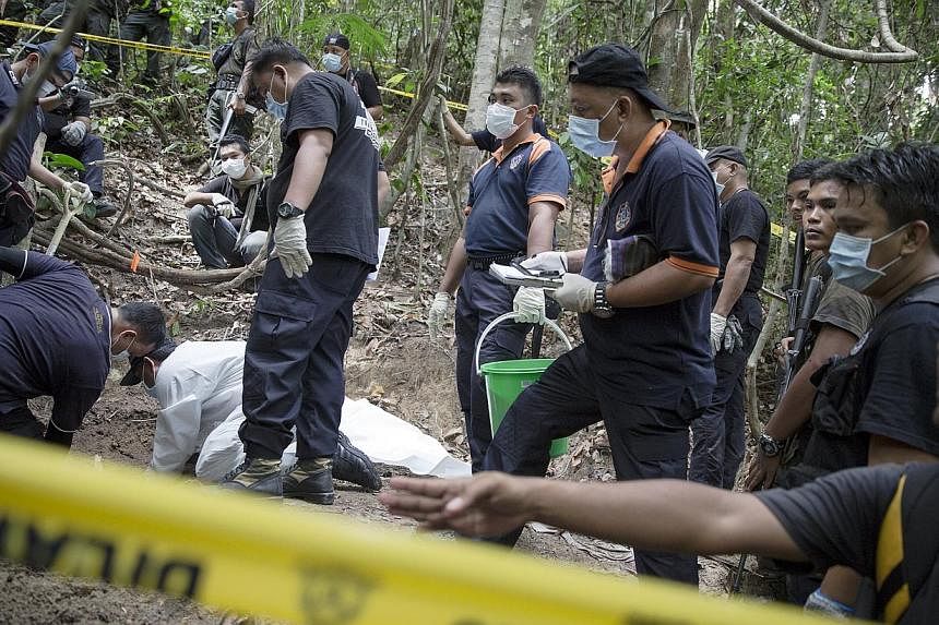 Policemen monitor as forensic experts dig out human remains near the abandoned human trafficking camp in the jungle close the Thailand border at Bukit Wang Burma in northern Malaysia May 26, 2015. -- PHOTO: REUTERS&nbsp;