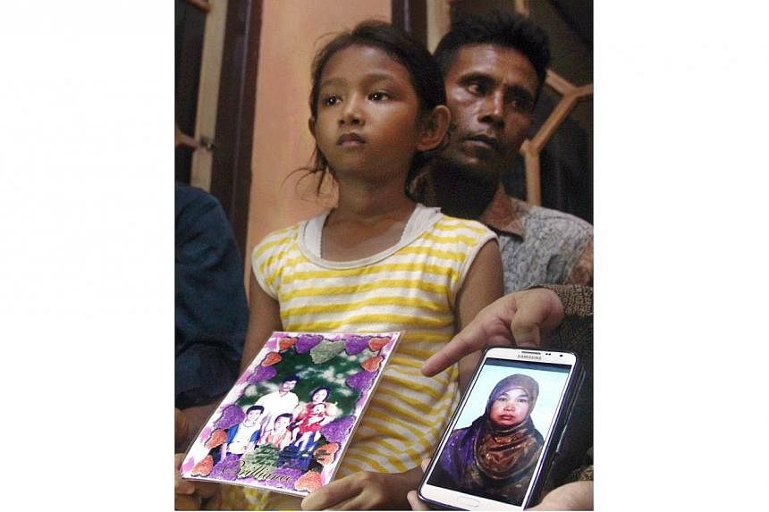 In this file photograph taken on April 17, 2015, Desi Sri Rahayu, the ten-year-old daughter of Karni binti Medi Tarsim, an Indonesian domestic worker executed in Saudi Arabia, holds her mother's family potrait as she sits with her father Darpin at th