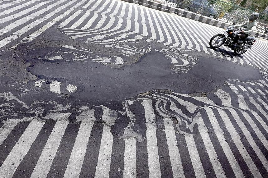 A motorcyclist rides past road markings that appear distorted due to the road asphalt melting and beginning to run, in New Delhi on May 27, 2015. Indian authorities have cancelled doctors' leave to help cope with the sick, as a heat wave spread acros