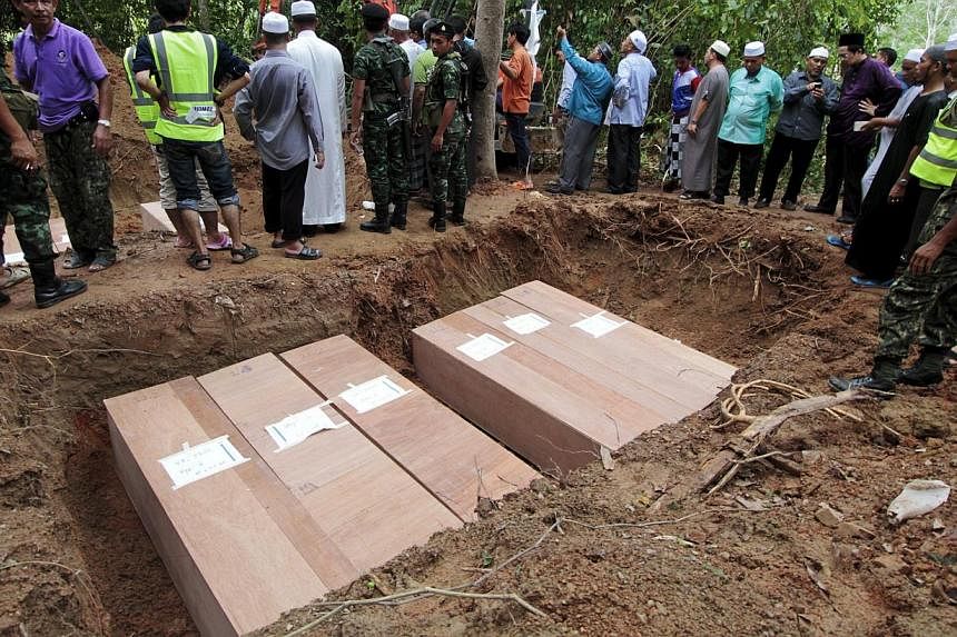 Thai Muslim villagers and security forces watch as coffins containing the remains of Rohingya migrants are placed in a grave for burial after a funeral at a graveyard in Thailand's southern Songkhla province on May 10, 2015. -- PHOTO: REUTERS