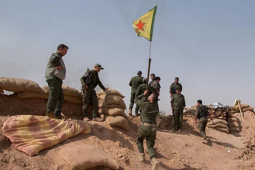 Kurdish People's Protection Unit (YPG) fighters raise a YPG flag over a barrier in Tel al-Aghbish village, which they said they retook control of from the Islamic State in Iraq and Syria (ISIS) on May 21, 2015. A group monitoring the war on Wednesday