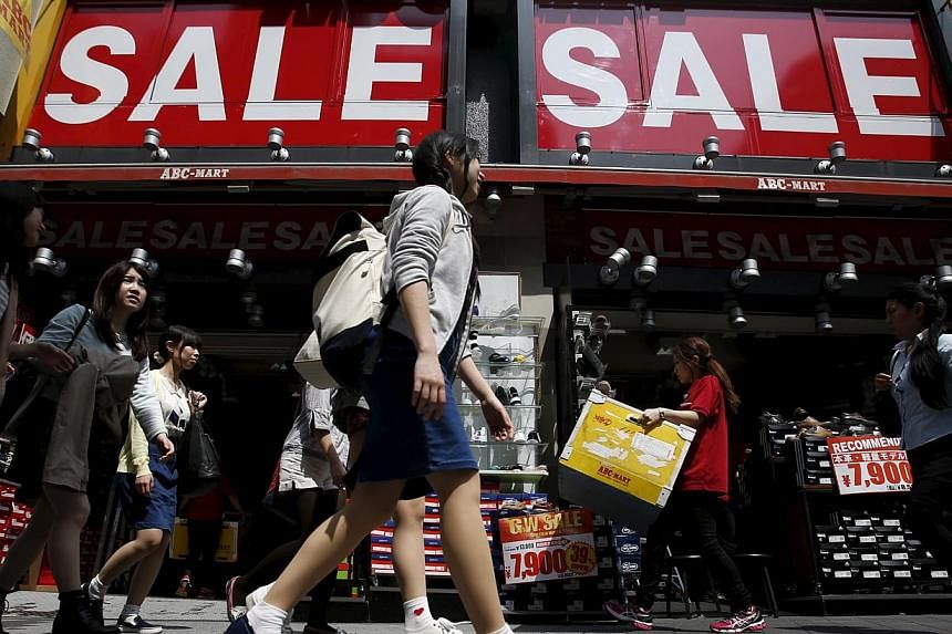 A shop clerk (second, right) carrying a box of shoes under sale signboards at a shoes retail store at a shopping district in Tokyo, Japan, on April 28, 2015. -- PHOTO: REUTERS