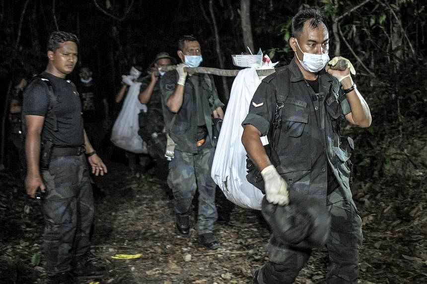 Royal Malaysian Police personnel carry exhumed human remains recovered from the jungle in the Malaysian northern state of Perlis, which borders Thailand, in Wang Kelian on May 28, 2015. -- PHOTO: AFP