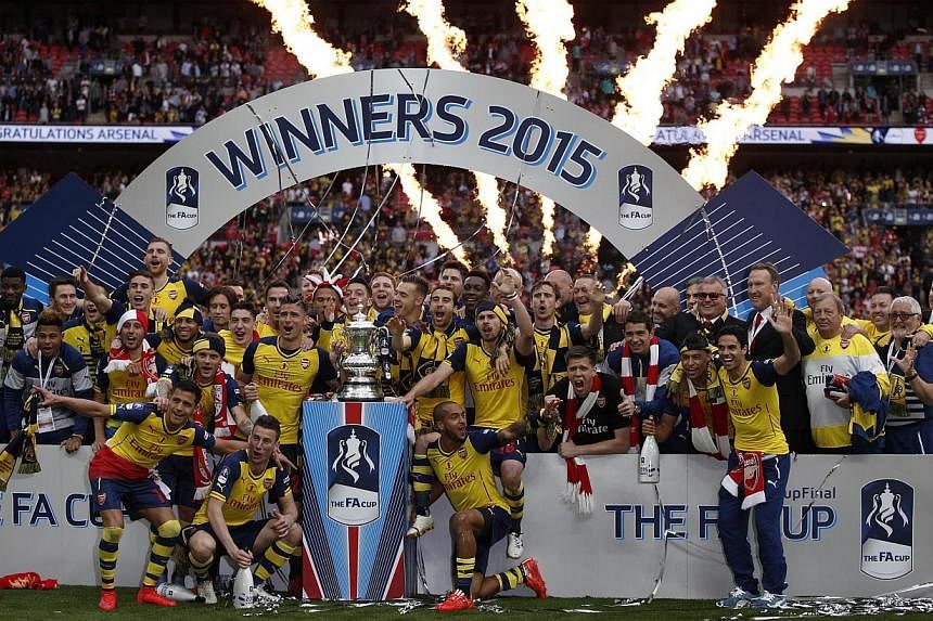 Arsenal manager Arsene Wenger (right) watches as his team celebrate with the trophy after winning the FA Cup final football match between Aston Villa and Arsenal at Wembley stadium in London on May 30, 2015. -- PHOTO: AFP