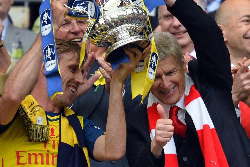 Arsenal manager Arsene Wenger (right) holding aloft the FA Cup trophy with defender Nacho Monreal after his team demolished Aston Villa 4-0 in the final at Wembley, London, on May 30, 2015. -- PHOTO: AFP