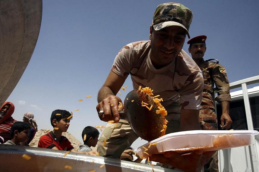 A member of the Iraqi government forces distributes food to displaced Iraqis who fled Anbar province due to the ongoing conflict between pro-government forces and Islamic State (IS) group jihadists, at a makeshift camp for internally displaced person