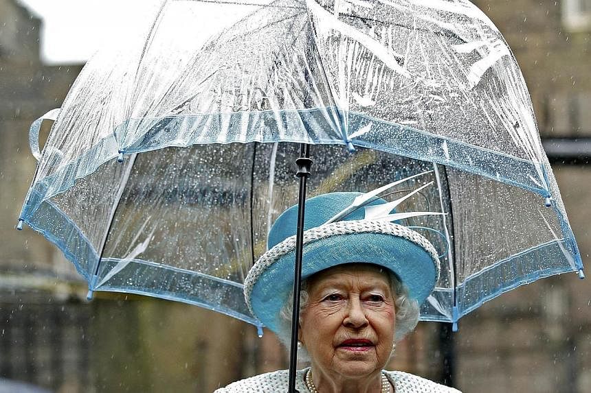 Britain's Queen Elizabeth II shelters from the rain beneath an umbrella as she arrives at Lancaster Castle in Lancaster, northern England on May 29, 2015. -- PHOTO: AFP&nbsp;