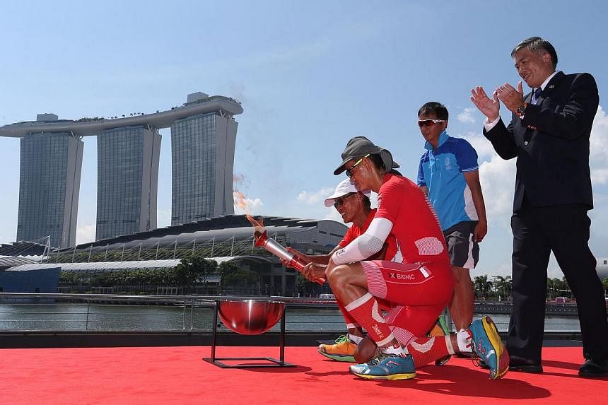Ultramarathoners Lim Nghee Huat and Yong Yuen Cheng lighting up the official SEA Games torch at The Promontory@Marina Bay. -- PHOTO: REUTERS