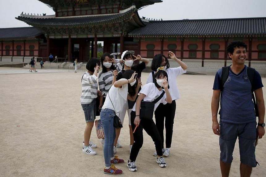 South Korean students wearing masks to protect against the Middle East Respiratory Syndrome (Mers) standing behind a tourist as he poses for photographs at the Gyeongbok Palace in central Seoul on June 4, 2015. -- PHOTO: REUTERS&nbsp;