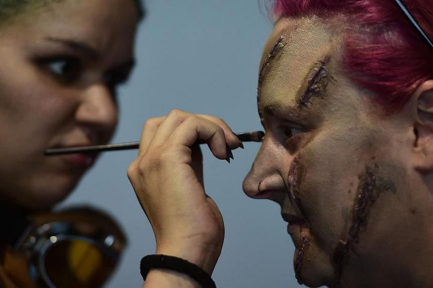 A woman (left) applying make-up to the face of a participant for the role game Survival Zombie in Olias del Rey on May 30, 2015. -- PHOTO: AFP