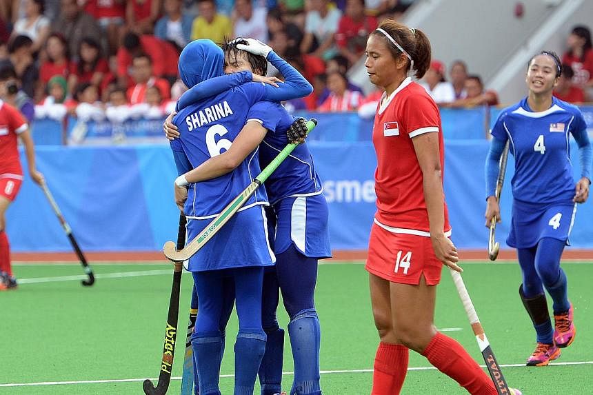 Singapore's Toh Limin walking past her jubilant Malaysian opponents after the women's hockey team was hammered 7-0 in their SEA Games opener at Sengkang hockey stadium on June 6, 2015. -- ST PHOTO: DESMOND WEE