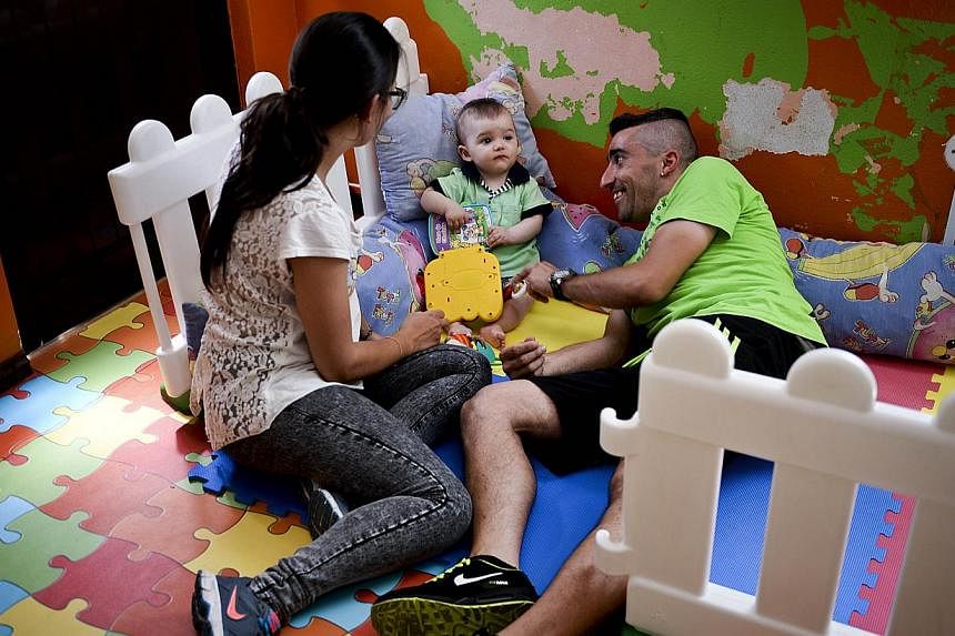 A file picture taken on May 14, 2015 shows Jessica (left) and her husband Antonio (right) playing with their child Martim born on August 8, 2014 at the kindergarten in Alcoutim, southern Portugal. The mayor of the small town of Alcoutim, in southern 