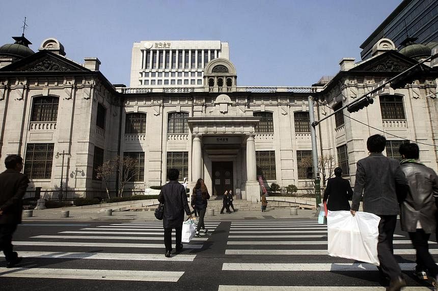Pedestrians cross a road in front of the Bank of Korea headquarters in Seoul, South Korea, on Monday, March 3, 2014. South Korea's central bank cut its policy rate by 25 basis points to a record-low 1.50 per cent on Thursday to offset any potentially