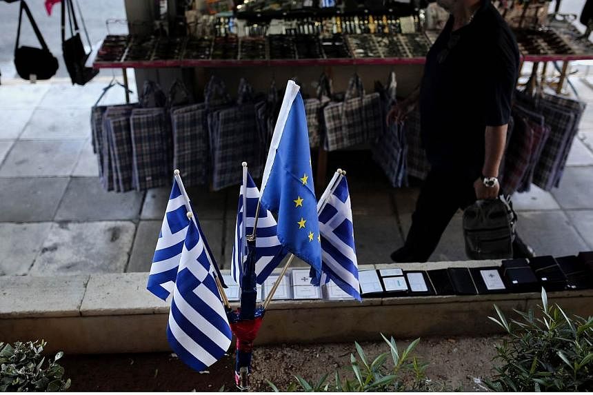 A man walks next to Greek national and European Union flags near the port of Piraeus on June 14, 2015.&nbsp;Greek and EU-IMF negotiators were locked in last-chance talks on Sunday to avert a default by Athens that could pave the way for a catastrophi