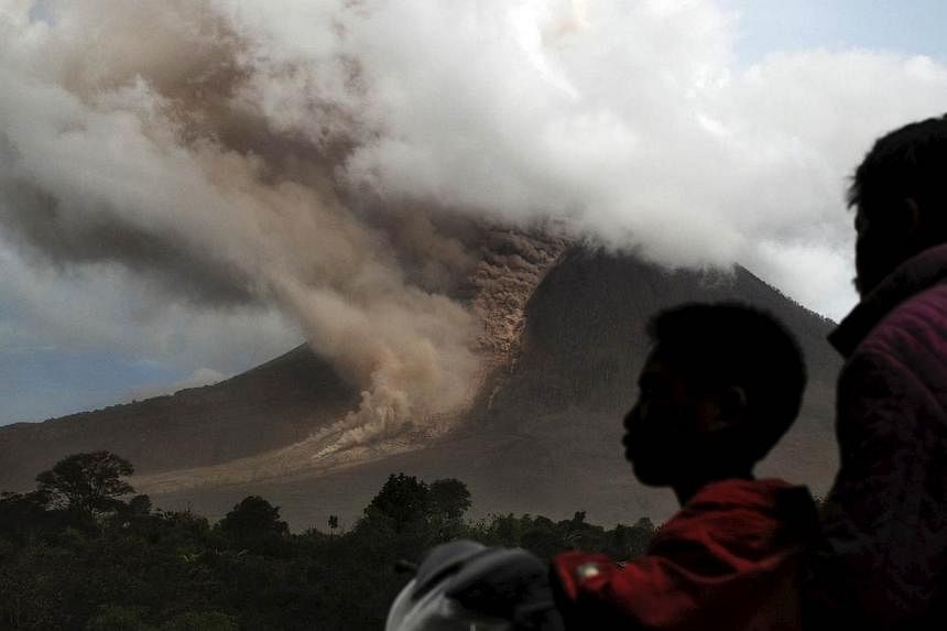 Residents sit on their motorcycle as they watch an eruption at Mount Sinabung, in Namanteran village in Karo Regency, Indonesia's North Sumatra province on June 14, 2015. -- PHOTO: REUTERS
