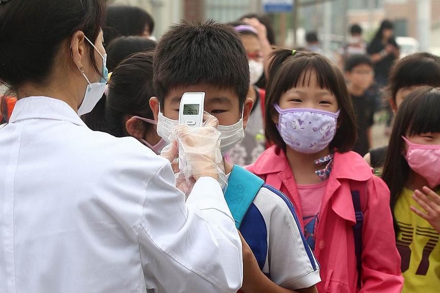 A health worker checks the body heat of children wearing face masks at an elementary school in Pyeongtaek, 65km south of Seoul, on June 15, 2015 as the school is reopened after a temporary closure in response to public fears over Middle East Respirat