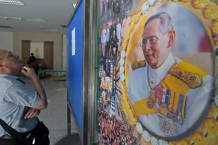 A Thai well-wisher reads a statment from the royal bureau next to a portrait of Thai King Bhumibol at Siriraj hospital in Bangkok on June 1, 2015. Thailand's junta has banned a journalists' association from holding a debate on controversial lese maje