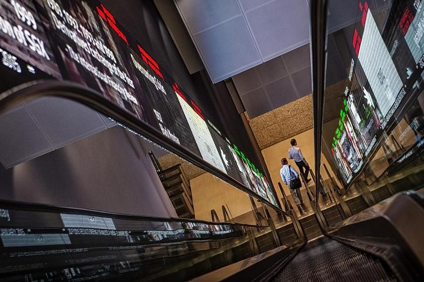 Pedestrians exit an escalator that runs past an electronic screen and ticker board that indicates stock figures at the Singapore Exchange (SGX) headquarters in Singapore, on Jan 21, 2015. -- PHOTO: BLOOMBERG&nbsp;