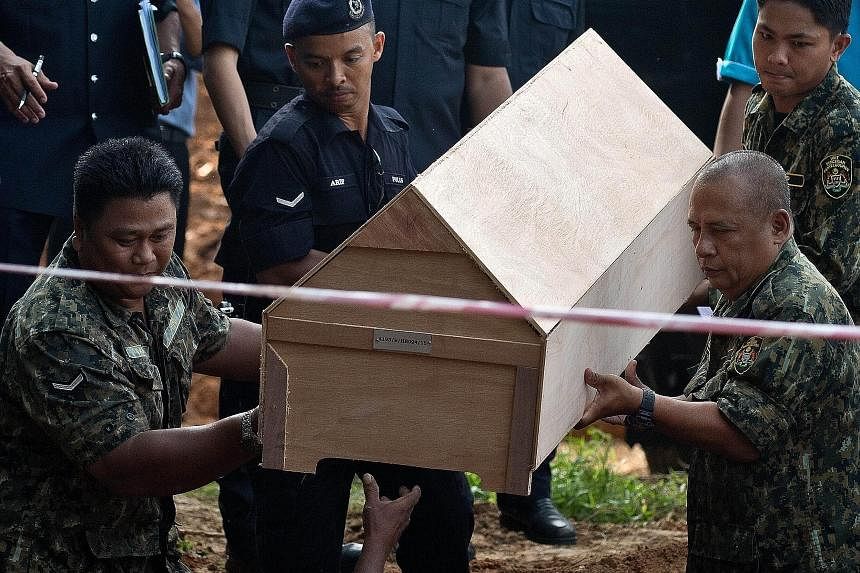 Workers in Kampung Tualang (above) preparing a pit yesterday for the reburial of remains believed to be those of Rohingya found at human-trafficking camps in jungles in northern Malaysia along the Thai border. (Left) Malaysian police and anti-smuggli