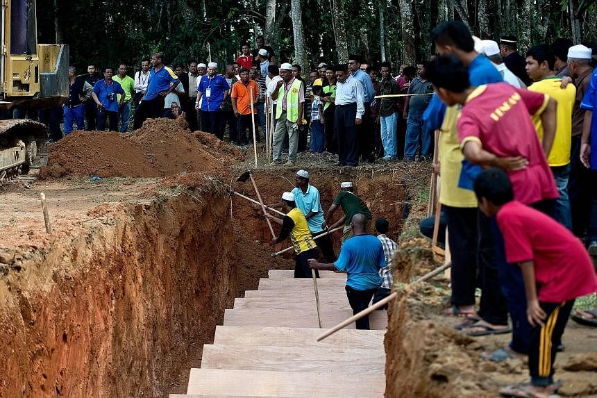 Workers in Kampung Tualang (above) preparing a pit yesterday for the reburial of remains believed to be those of Rohingya found at human-trafficking camps in jungles in northern Malaysia along the Thai border. (Left) Malaysian police and anti-smuggli