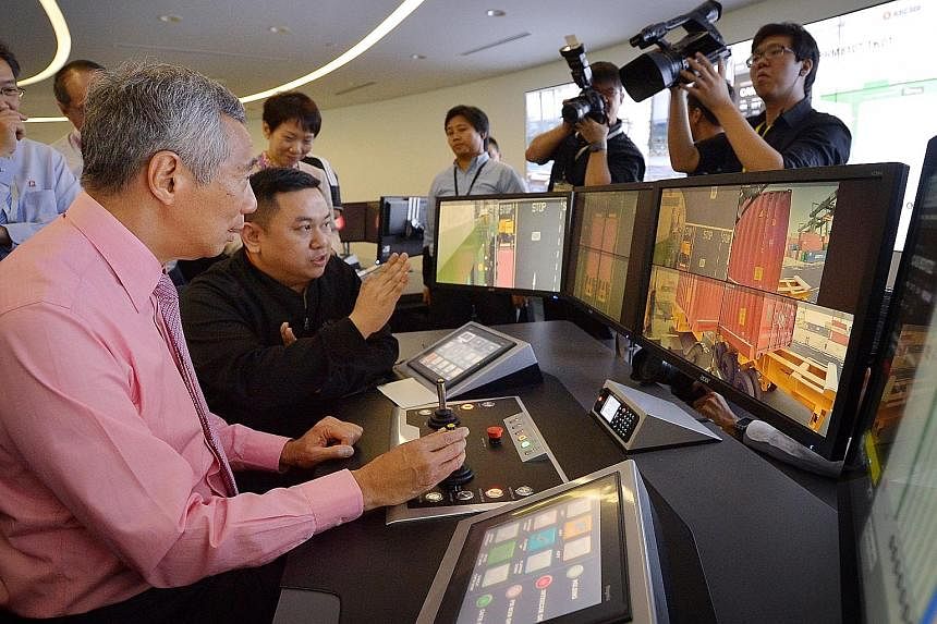 PM Lee Hsien Loong operating a crane from the Automated Crane Operations Centre, guided by assistant operations executive Larry Wong (seated, in black), yesterday. The cranes, which can be operated remotely, help save on manpower and increase product