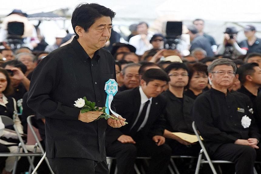 Japanese Premier Shinzo Abe offering a flower at a ceremony to remember the Battle of Okinawa yesterday, as Okinawa Governor Takeshi Onaga (right) looked on. There were cries for Mr Abe to "go home". Residents of the island, which suffered Japan's on