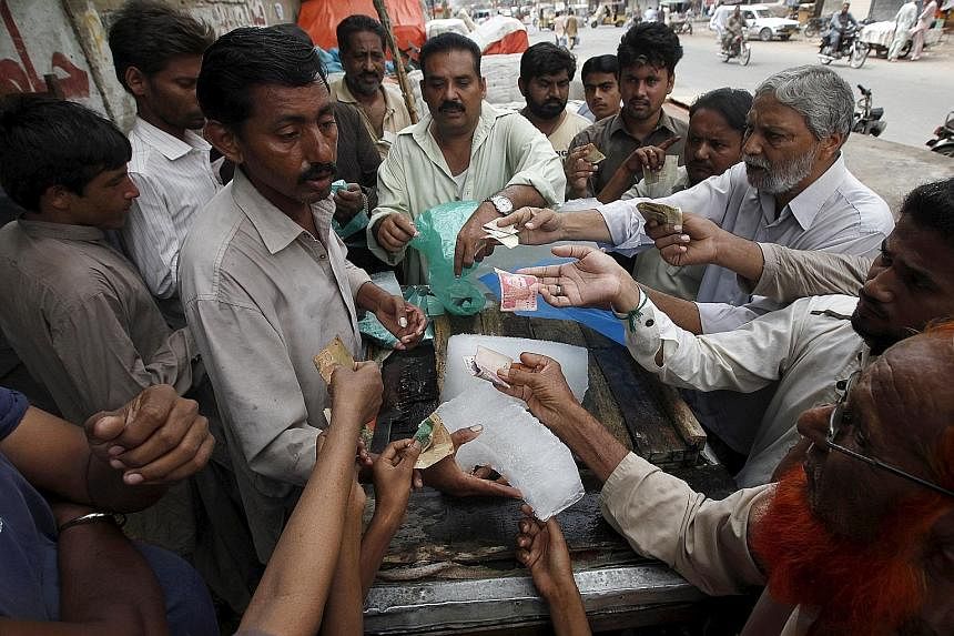 People buying ice blocks from a roadside vendor in Karachi. Ice is in short supply and is sold at a premium in many neighbourhoods. The hot weather is expected to last until the end of the month.