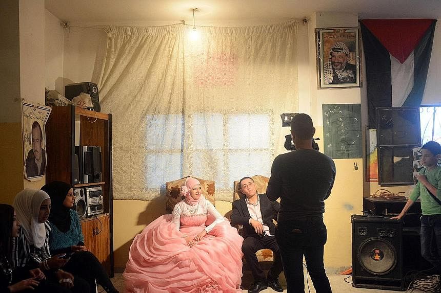 A videographer filming a wedding couple in an apartment. On the wall is a Palestine flag as well as a picture of the late Palestinian leader Yasser Arafat.