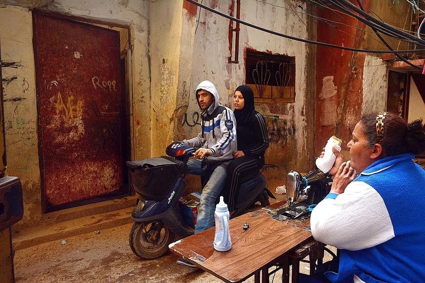 A scooter passing a resident eating outside her home. Unemployment is high as refugees are discriminated against in the Lebanese job market.